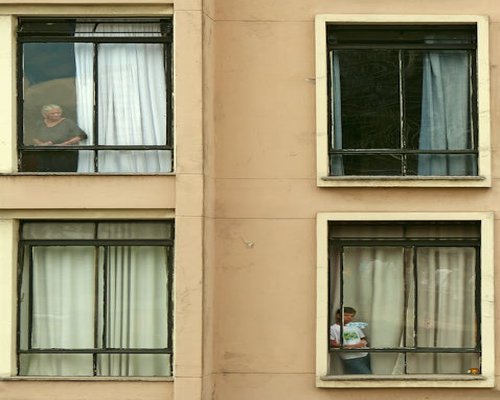 Mujer mirando por la ventana de su departamento tomando un descanso
